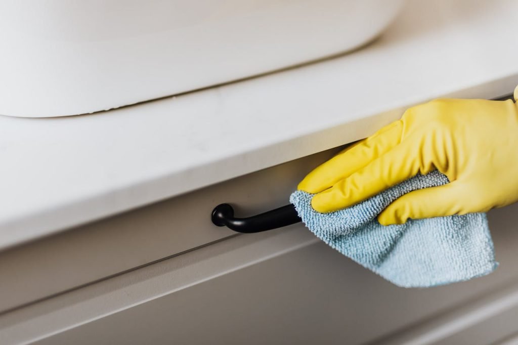 crop-housekeeper-cleaning-handle-with-rag-4239032 From above of crop faceless person in yellow gloves cleaning handle of cabinet with microfiber cloth in modern bright bathroom